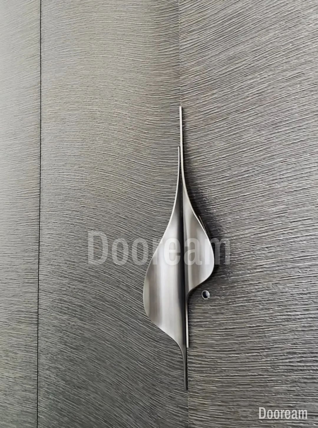 Grey brushed-texture leaves set flush in a matching wall, with a sculpted steel pull shaped like a sail across the seam.